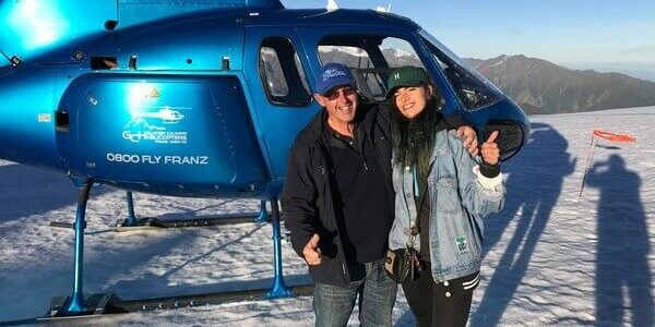 John Funnell with his arm around a women standing in front of a blue helicopter